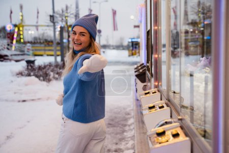 Foto de Mujer alegre y elegante, vestida con ropa de abrigo, se divierte en un parque de atracciones de invierno nevado. - Imagen libre de derechos