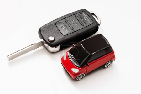 Téléchargez les photos : Jouet voiture rouge avec toit noir à côté d'une clé de voiture noire sur fond blanc. Mettre l'accent sur la clé. - en image libre de droit