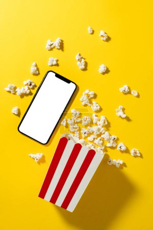 Téléchargez les photos : Seau popcorn classique et smartphone avec écran blanc sur fond jaune. - en image libre de droit