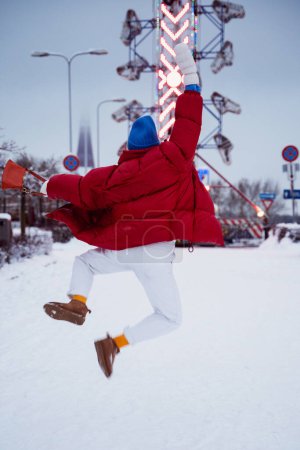 Photo for Cheerful and stylish woman, dressed in warm clothes, is having fun in a snowy winter amusement park. - Royalty Free Image