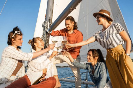 Téléchargez les photos : Groupe d'amis heureux boire du vin et se détendre sur le voilier pendant la voile en mer. - en image libre de droit
