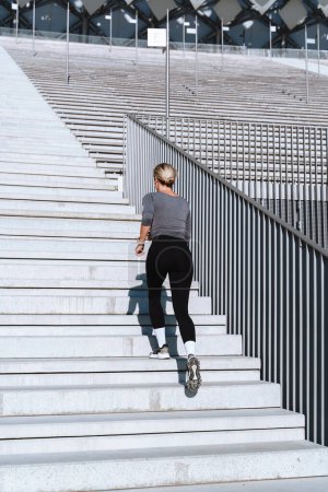 Photo for Woman athlete wearing female sportswear running and  exercising on staircase between bleachers of outdoor stadium. - Royalty Free Image