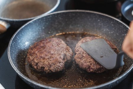 Photo for Juicy ground beef hamburger patty sizzling and cooking to perfection inside a frying pan. - Royalty Free Image