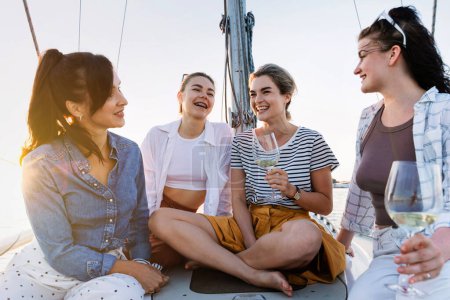 Photo for Happy girls friends drinking white wine on the sailboat during sailing in the sea. - Royalty Free Image