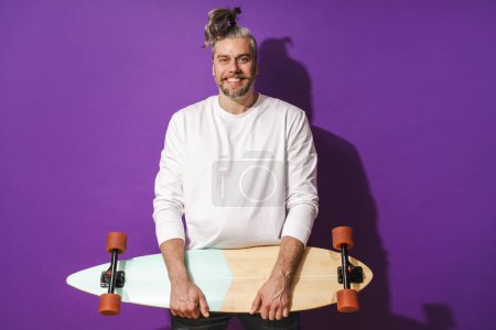 Photo for Portrait of cheerful middle aged man with longboard wearing white sweatshirt against purple background - Royalty Free Image