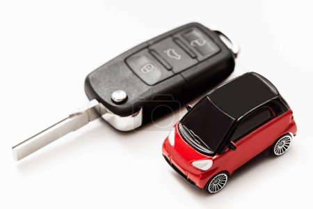 Téléchargez les photos : Jouet voiture rouge avec toit noir à côté d'une clé de voiture noire sur fond blanc. Focus sur la voiture. - en image libre de droit