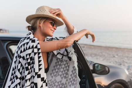 Téléchargez les photos : Voyageur femme prendre une pause par sa voiture sur une plage de galets. - en image libre de droit