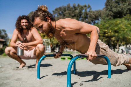 Photo for Two young men exercising on the bars during beach training - Royalty Free Image