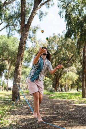 Photo for Confident young man juggling and balancing on the slackline in city park during summer day - Royalty Free Image