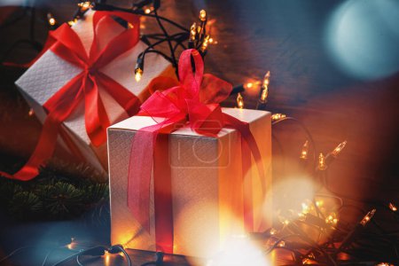 Photo for Wrapped gift boxes with vibrant red ribbons, nestled among twinkling Christmas lights and fresh spruce twigs. - Royalty Free Image