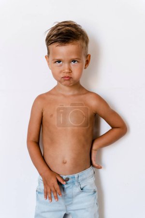 Photo for Cute little boy wearing blue jeans posing against white background with silly facial expression. - Royalty Free Image