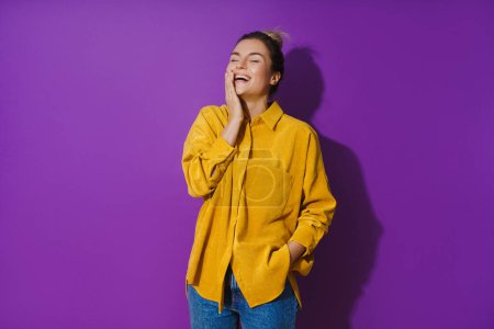 Photo for Portrait of young cheerful laughing girl wearing yellow shirt against purple background - Royalty Free Image