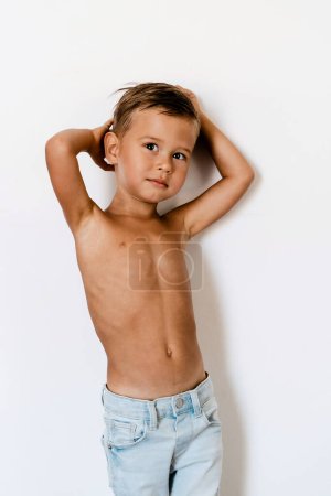Téléchargez les photos : Mignon petit garçon portant un jean bleu posant sur fond blanc comme un mannequin. - en image libre de droit