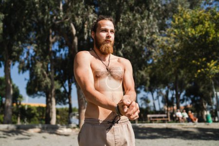 Photo for Young bearded man warming up before his workout on the beach - Royalty Free Image