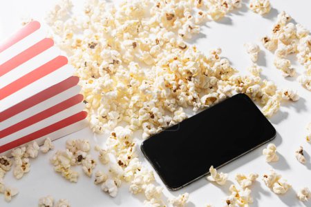 Photo for Classic popcorn bucket and smartphone with blank screen on white background. - Royalty Free Image