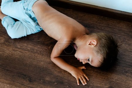 Téléchargez les photos : Portrait de petit garçon maigre et triste couché sur le sol - en image libre de droit