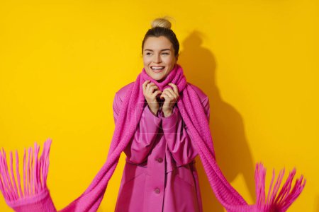Foto de Retrato de una joven mujer alegre con abrigo rosa y bufanda de lana sobre fondo amarillo - Imagen libre de derechos