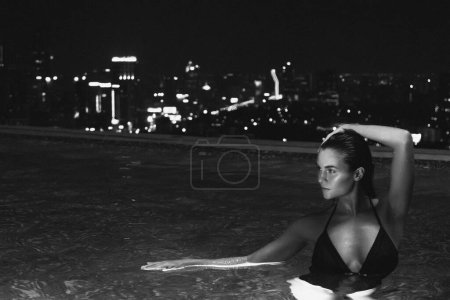Photo for Monochrome image with noise effect of young gorgeous woman in infinity swimming pool on the roof on tall building - Royalty Free Image