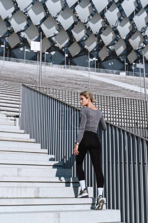 Photo for Woman athlete wearing female sportswear climbing stairs of outdoor stadium. - Royalty Free Image