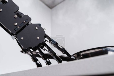 Foto de Auténtica mano robot y sartén en estufa eléctrica. Concepto de automatización robótica de procesos. - Imagen libre de derechos