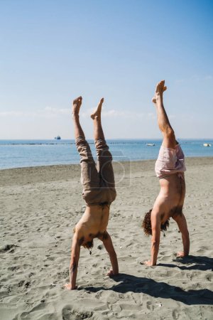 Foto de Dos hombres haciendo handstand para la fuerza y el equilibrio en la playa de arena - Imagen libre de derechos