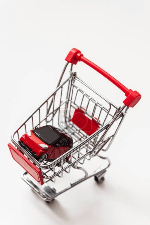 Photo for Red toy car inside small shopping cart on white background - Royalty Free Image