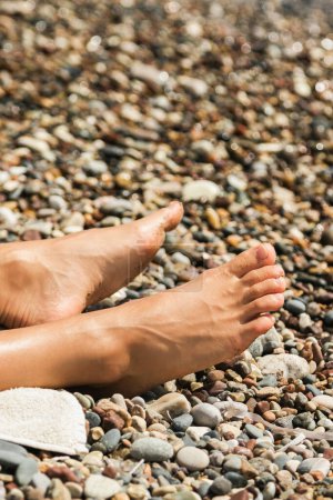 Téléchargez les photos : Gros plan pieds féminins pendant la journée ensoleillée à la plage de galets - en image libre de droit