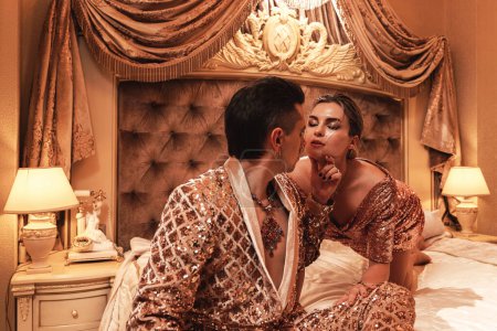 Foto de Riqueza joven pareja está vestida con trajes dorados radiantes adornados con bordados de lentejuelas, situado en una lujosa suite. - Imagen libre de derechos
