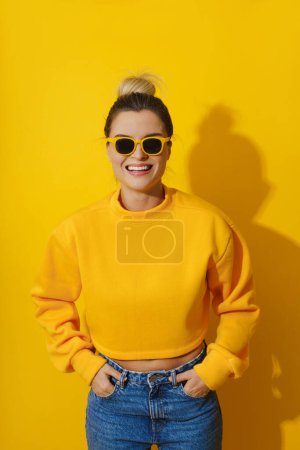 Foto de Retrato de niña alegre con sudadera amarilla y gafas de sol sobre fondo amarillo - Imagen libre de derechos
