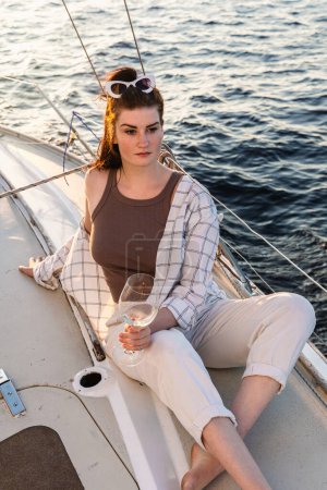 Téléchargez les photos : Belle femme buvant du vin et se relaxant sur voilier pendant la voile en mer. - en image libre de droit
