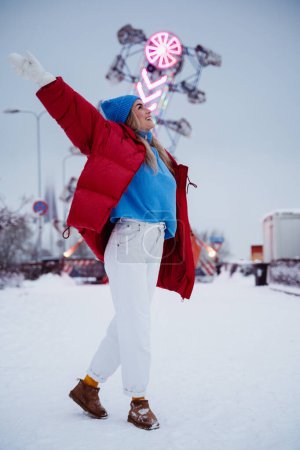 Téléchargez les photos : Femme gaie et élégante, vêtue de vêtements chauds, s'amuse dans un parc d'attractions hivernal enneigé. - en image libre de droit