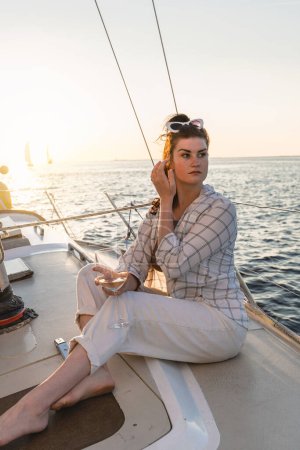 Téléchargez les photos : Belle femme buvant du vin et se relaxant sur voilier pendant la voile en mer. - en image libre de droit