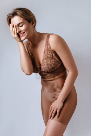 Foto de Retrato de mujer atractiva joven con sujetador de encaje marrón y calzoncillos de cintura alta sobre fondo gris. - Imagen libre de derechos