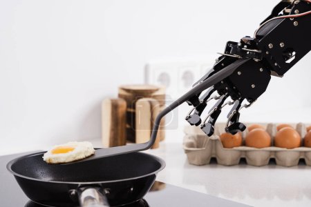Téléchargez les photos : Véritable robot main et poêle à frire avec œuf frit. Concepts du développement de l'IA et de l'automatisation robotique des processus. - en image libre de droit