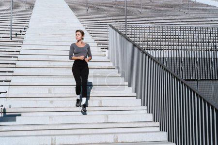 Téléchargez les photos : Athlète femme portant des vêtements de sport féminins courant et faisant de l'exercice sur un escalier entre les gradins du stade extérieur. - en image libre de droit