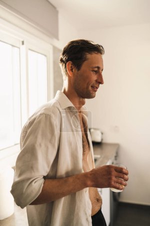 Photo for Portrait of attractive male slob drinking whiskey in his kitchen - Royalty Free Image