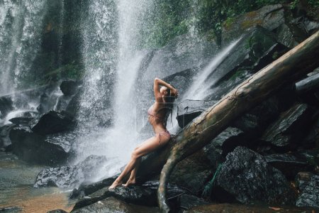 Photo for Gorgeous wet woman posing beside mighty Phnom Kulen waterfall in Cambodia - Royalty Free Image