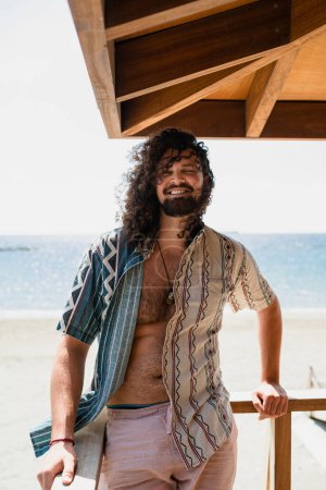 Foto de Retrato del hombre rizado despreocupado relajándose en la playa durante el día soleado de verano - Imagen libre de derechos