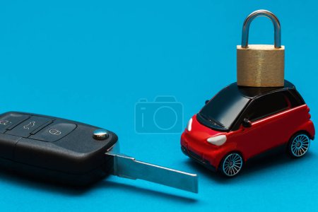 Foto de Una foto de cerca con fondo azul de una llave de coche negro en el lado izquierdo y un coche rojo juguete con cerradura metálica amarilla en el techo - Imagen libre de derechos