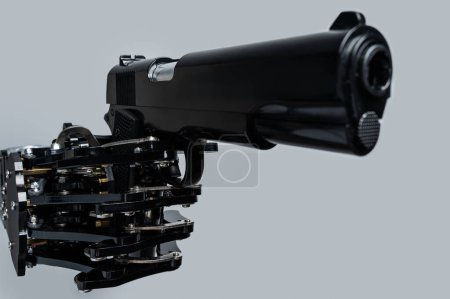 Téléchargez les photos : Une vraie main de robot avec une arme de poing. Concept de prise de contrôle de l'IA et singularité technologique. - en image libre de droit