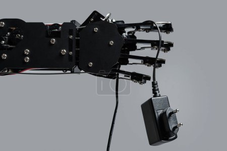 Téléchargez les photos : Véritable main robotique avec adaptateur secteur. Concepts de la prise de contrôle par l'IA et singularité technologique. - en image libre de droit