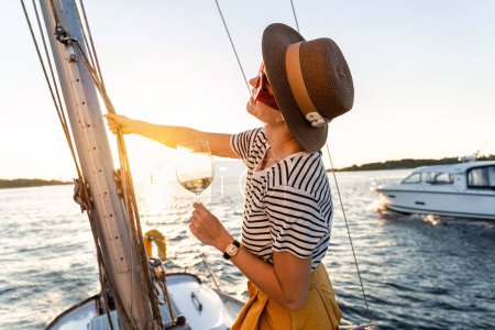 Téléchargez les photos : Joyeux jeune femme boire du vin et se détendre sur le voilier pendant la voile en mer. - en image libre de droit