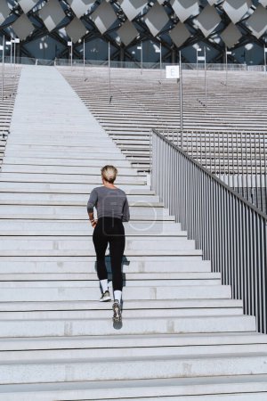 Foto de Mujer atleta con ropa deportiva femenina corriendo y ejercitándose en la escalera entre gradas del estadio al aire libre. - Imagen libre de derechos