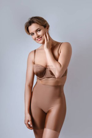 Foto de Retrato de mujer atractiva joven con lencería marrón con calzoncillos de cintura alta sobre fondo gris. - Imagen libre de derechos