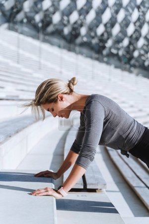 Photo for Woman athlete wearing female sportswear doing push-ups during calisthenic workout on staircase of outdoor stadium. - Royalty Free Image