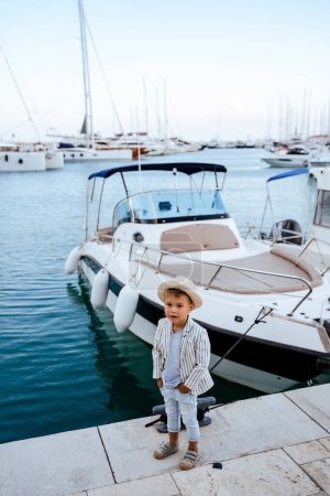 Téléchargez les photos : Portrait de garçon élégant mignon posant près du yacht dans la marina - en image libre de droit
