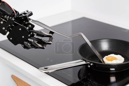 Téléchargez les photos : Véritable robot main et poêle à frire avec œuf frit. Concepts du développement de l'IA et de l'automatisation robotique des processus. - en image libre de droit