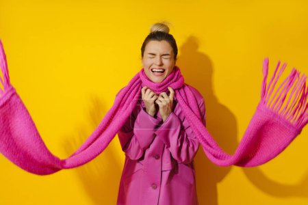 Photo for Portrait of young cheerful woman wearing pink coat and wool scarf against yellow background - Royalty Free Image