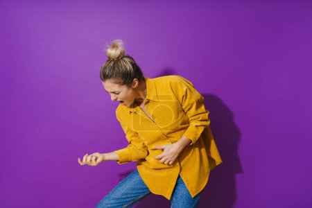 Téléchargez les photos : Portrait de jeune fille joyeuse portant chemise jaune jouant de la guitare à air sur fond violet - en image libre de droit