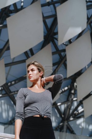 Foto de Mujer atleta confiada usando ropa deportiva femenina posando contra el fondo futurista moderno. - Imagen libre de derechos